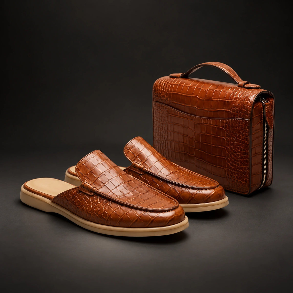 A pair of brown crocodile-embossed slip-on loafers with beige soles, displayed alongside a matching brown crocodile-embossed leather travel or briefcase-style bag with a top handle and zipper, set against a dark gray studio background.